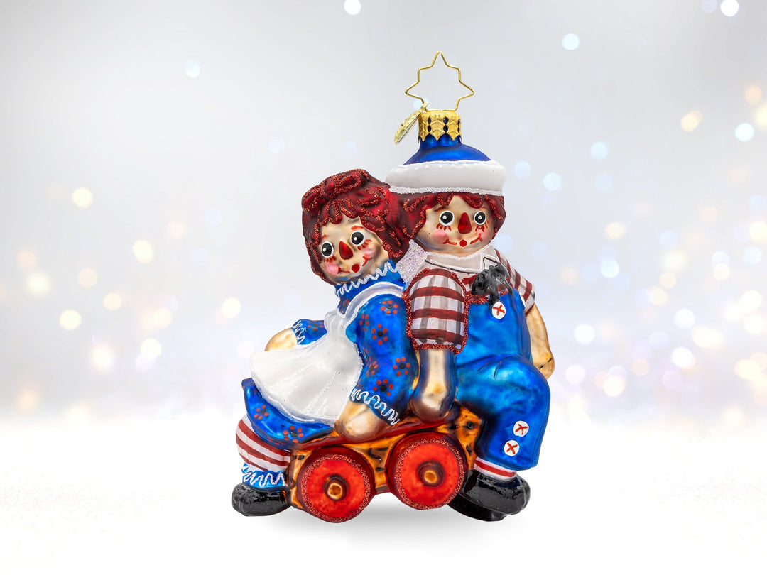 A Raggedy Ann and Andy Ornament sitting back to back on a toy wagon.