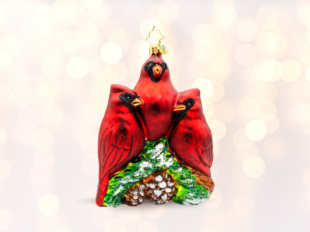 An ornament of three red cardinal birds sitting on part of a snowy tree top.