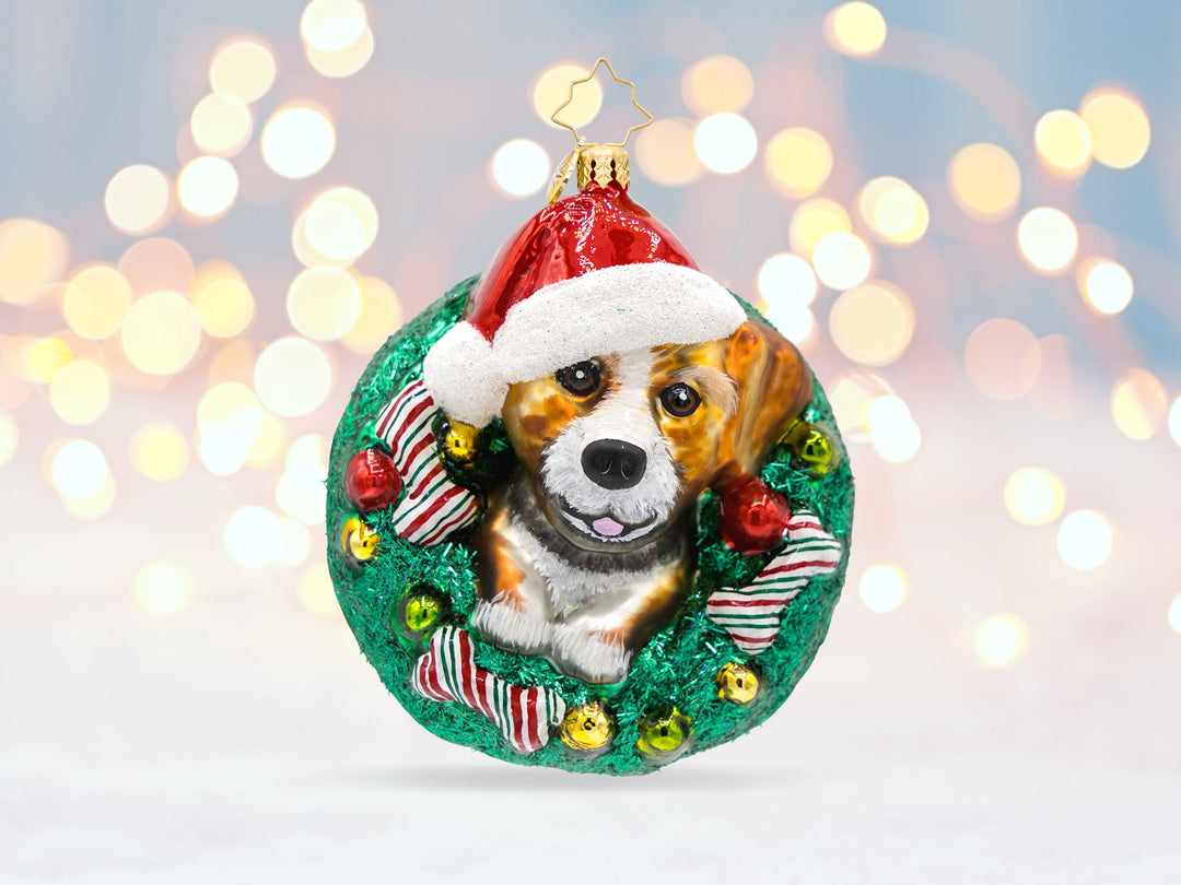 A dog ornament featuring a dog's front on a green wreath with red and green striped dog bones.