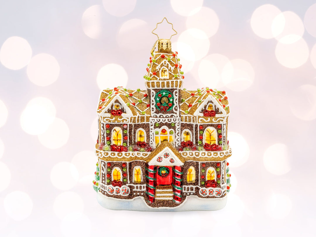 A gingerbread home ornament, fully decorated with frosting, Christmas lights, and wreaths.