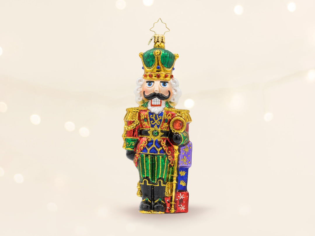A red and green nutcracker ornament wearing a gold and green crown, and holding a gold cane.