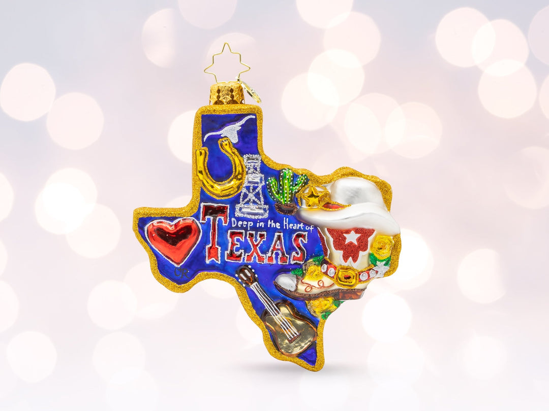A blue and gold ornament in the shape of Texas with a horshoe, oil drill, cactus, cowboy hat, guitar, and heart on the ornament representing the state.