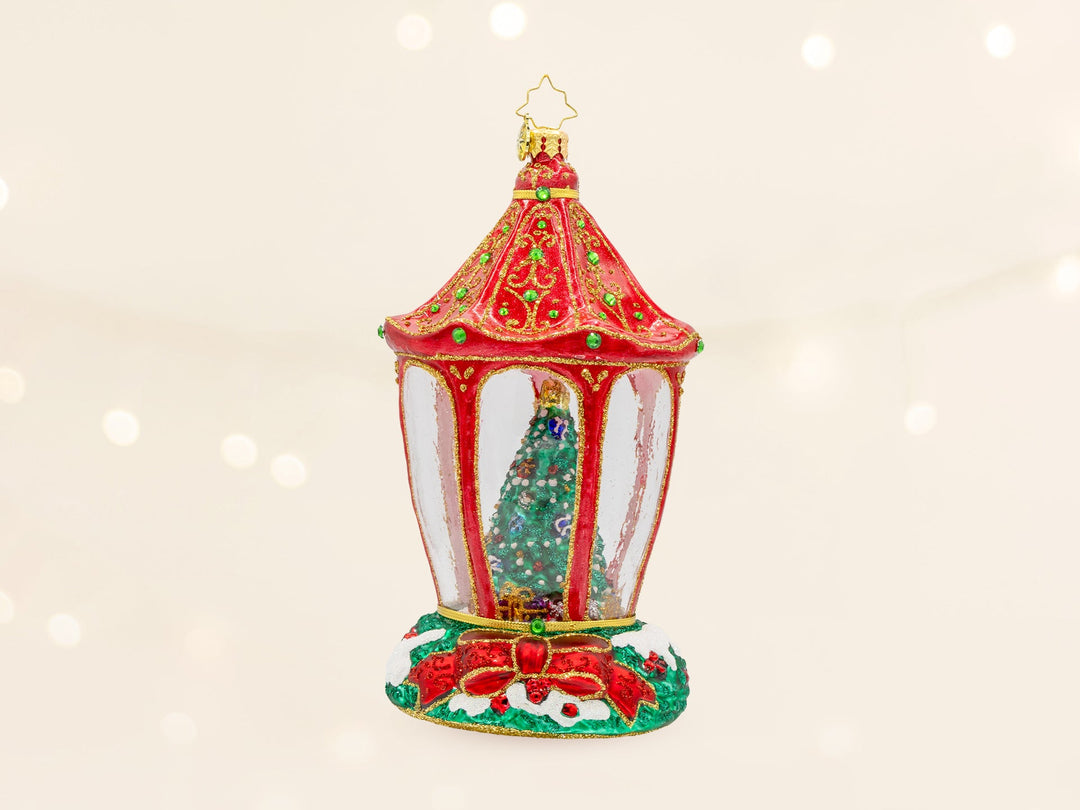 A green Christmas tree contained in a red lattern ornament with a red ribbon at the base.