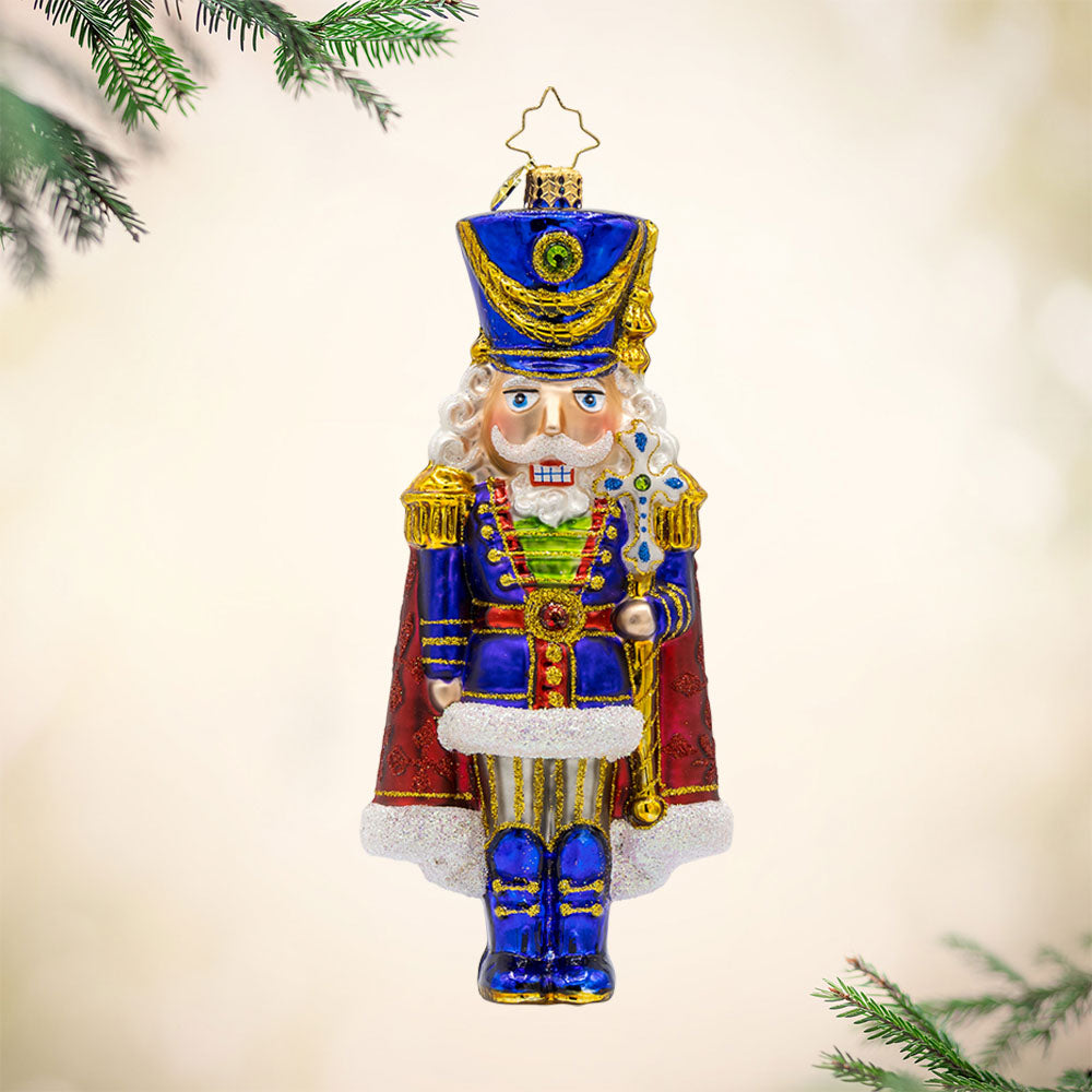 Long Coat Nutcracker ornament. Features elegant attire of regal blue and red accompanied by a dignified stance. View of front.