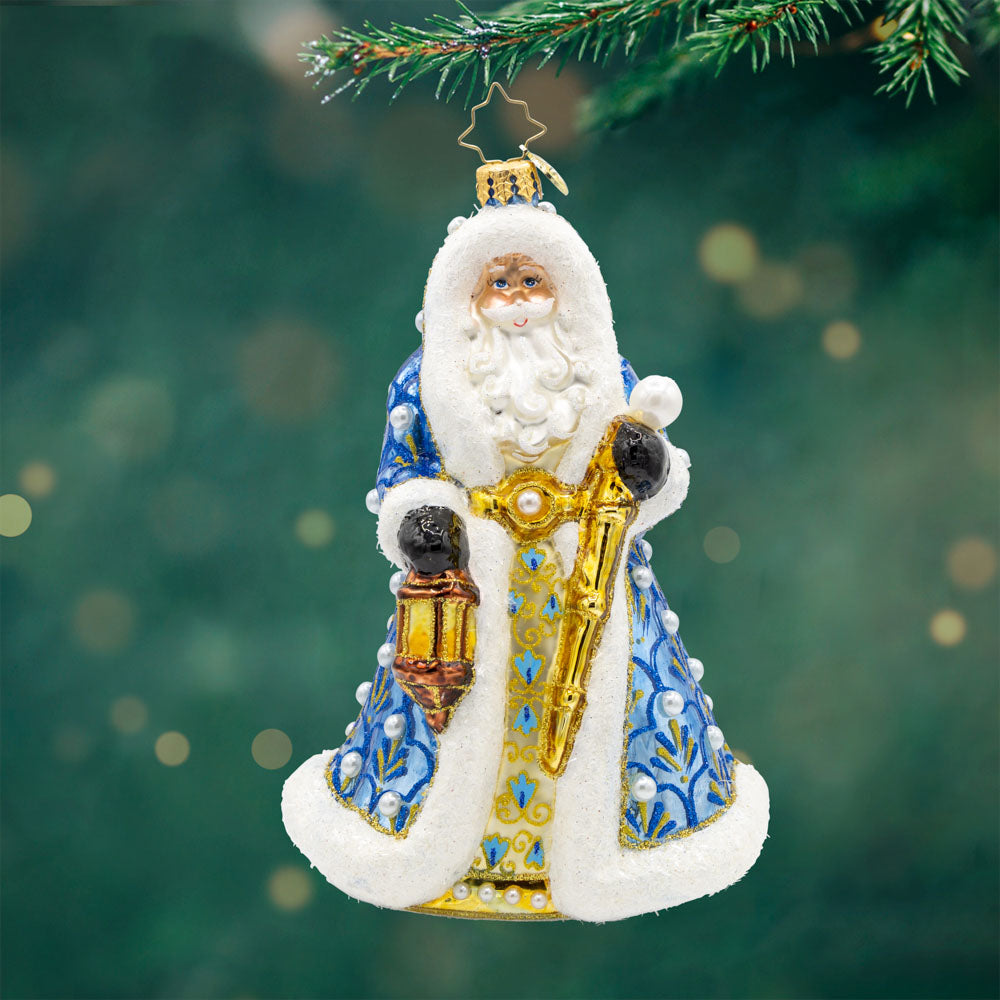 Gilded Grandeur Santa ornament. Dressed in a blue satin coat adorned with intricate designs, paired with his shiny staff and a lantern that casts a warm glow. View of front.