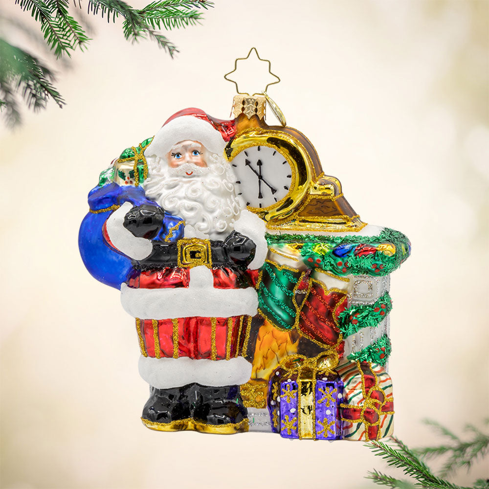 A Warm Santa by Fireplace ornament. Santa is taking a break, enjoying a cozy fire surrounded by festive goodies. View of front.