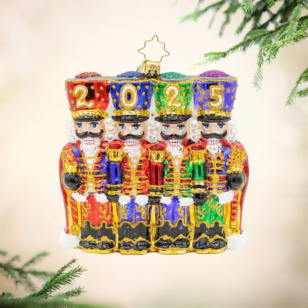 2025 Marching Guardians ornament. This ornament features a row of nutcrackers, with their shiny hats, sparkling sabers, and colorful costumes. "2025" is written across their hats. View of front.
