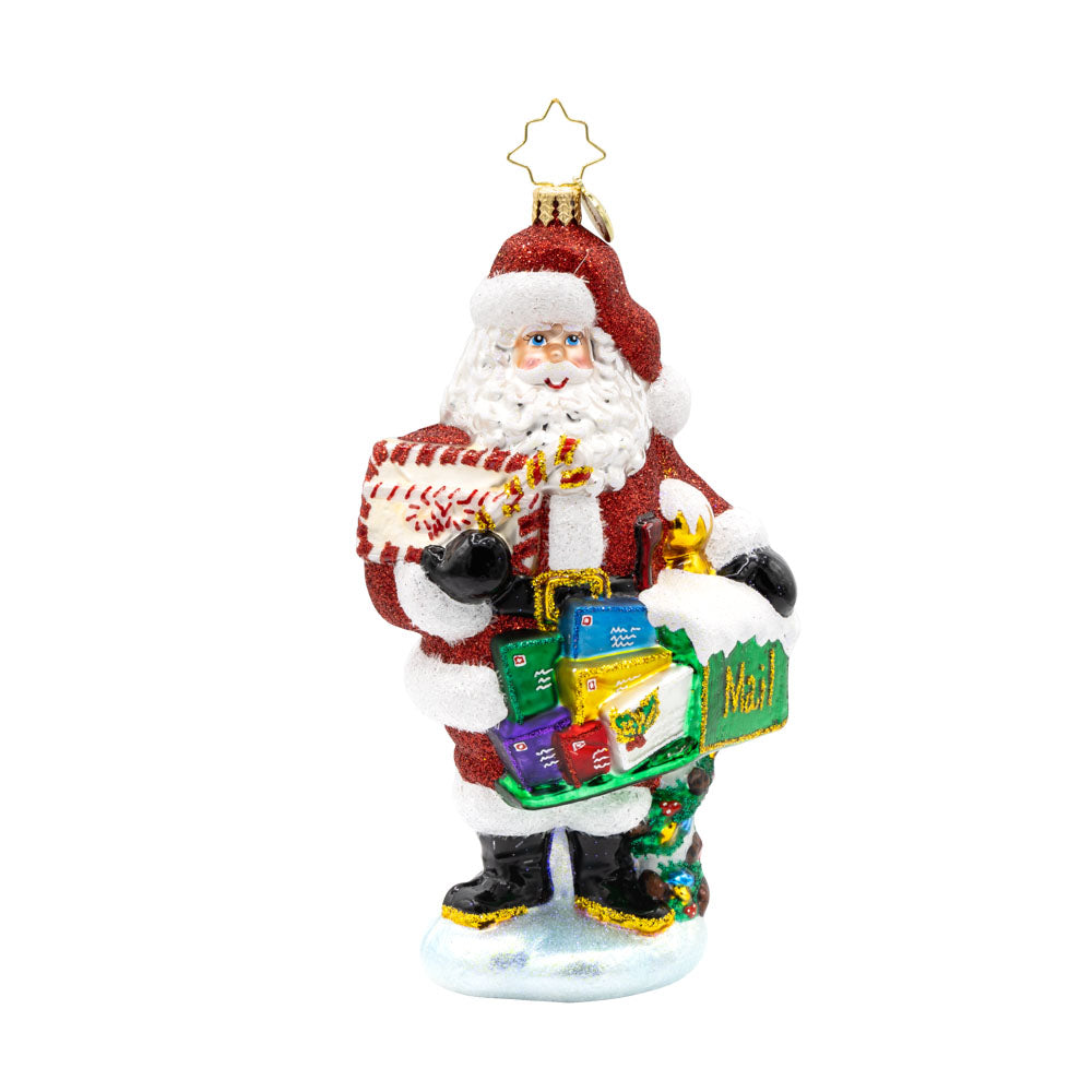 North Pole Mail Delivery ornament. Santa dons his red suit, standing next to a green mailbox filled with letters. View of front.