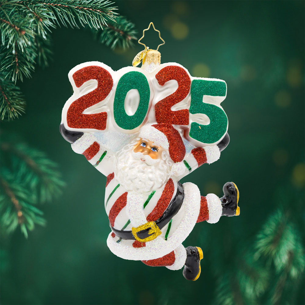 Peppermint St. Nick Ornament.  Santa is dressed in a peppermint-striped suit, complete with a shiny hat, mittens, and a touch of glitter. "2025" is held above his head in similar colors. View of front.