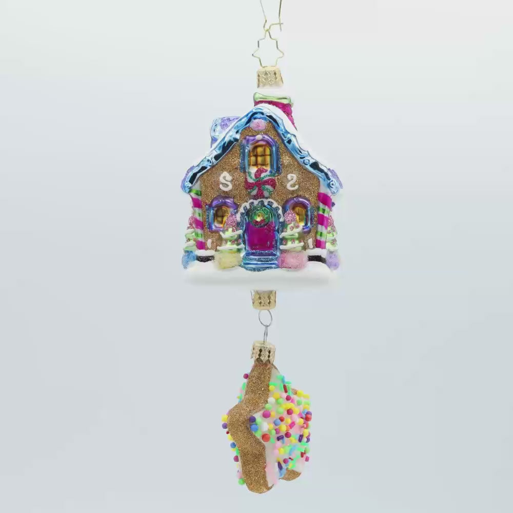 Sweet Beginnings ornament. A gingerbread house decorated in vibrant colors and candy. A gingerbread star cookie covered in sprinkles hangs below. Video.