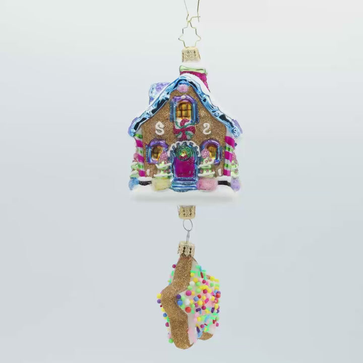 Sweet Beginnings ornament. A gingerbread house decorated in vibrant colors and candy. A gingerbread star cookie covered in sprinkles hangs below. Video.