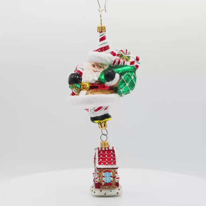 Ornament features a gingerbread house dangling from Santa's feet. Santa is holding a bag overflowing with treats. Video.