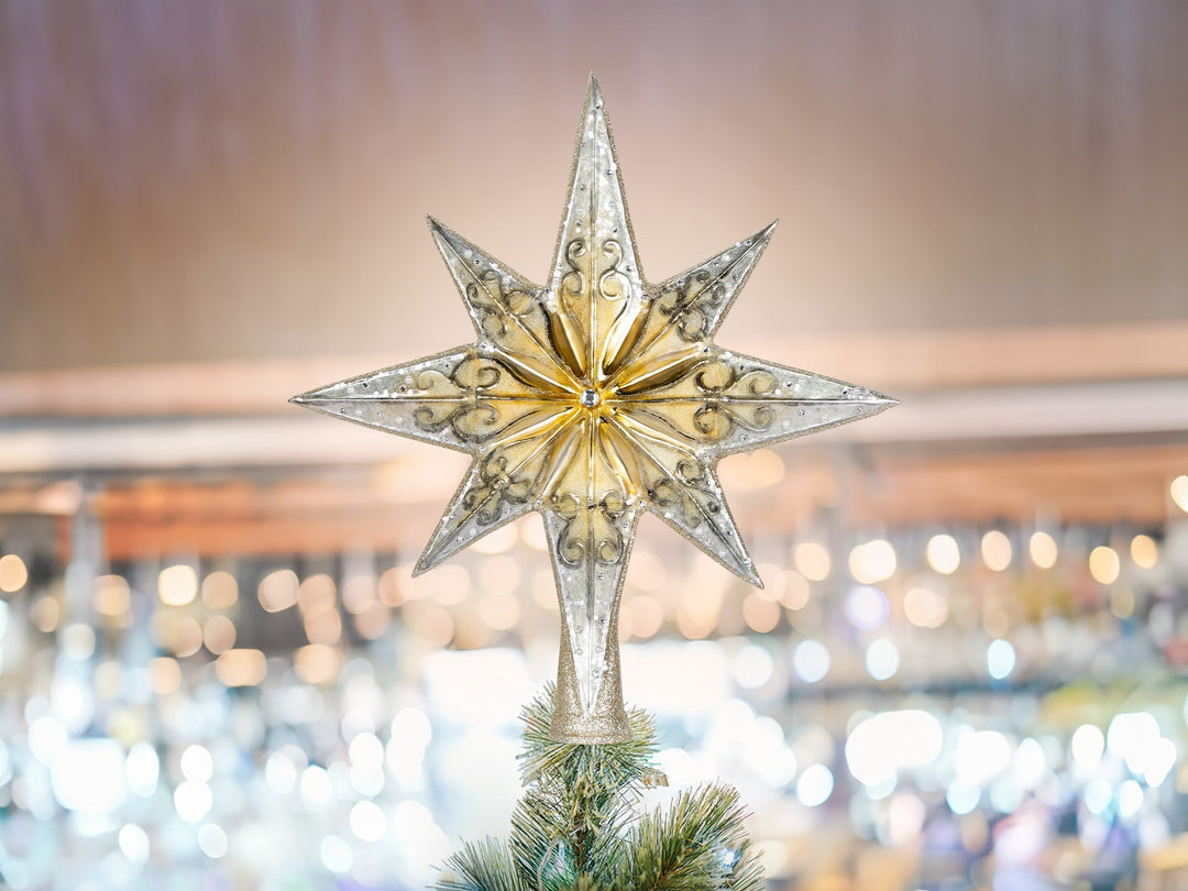 A white and gold star finial sitting on top of a Christmas tree.
