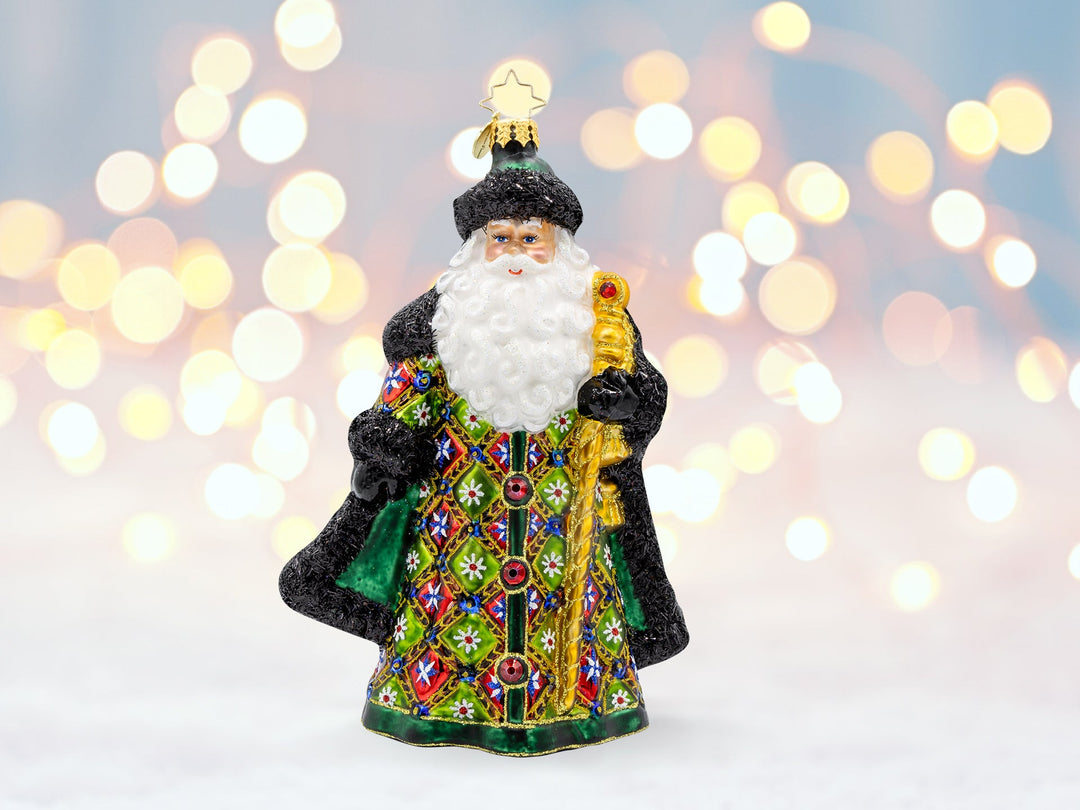 A red, green, and black traditional robed santa ornament, and is holding a gold cane.