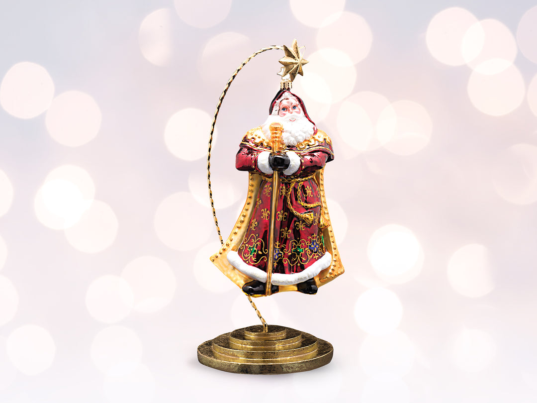 A robed santa wearing a cape and robe ornament hanging from a gold ornament stand.