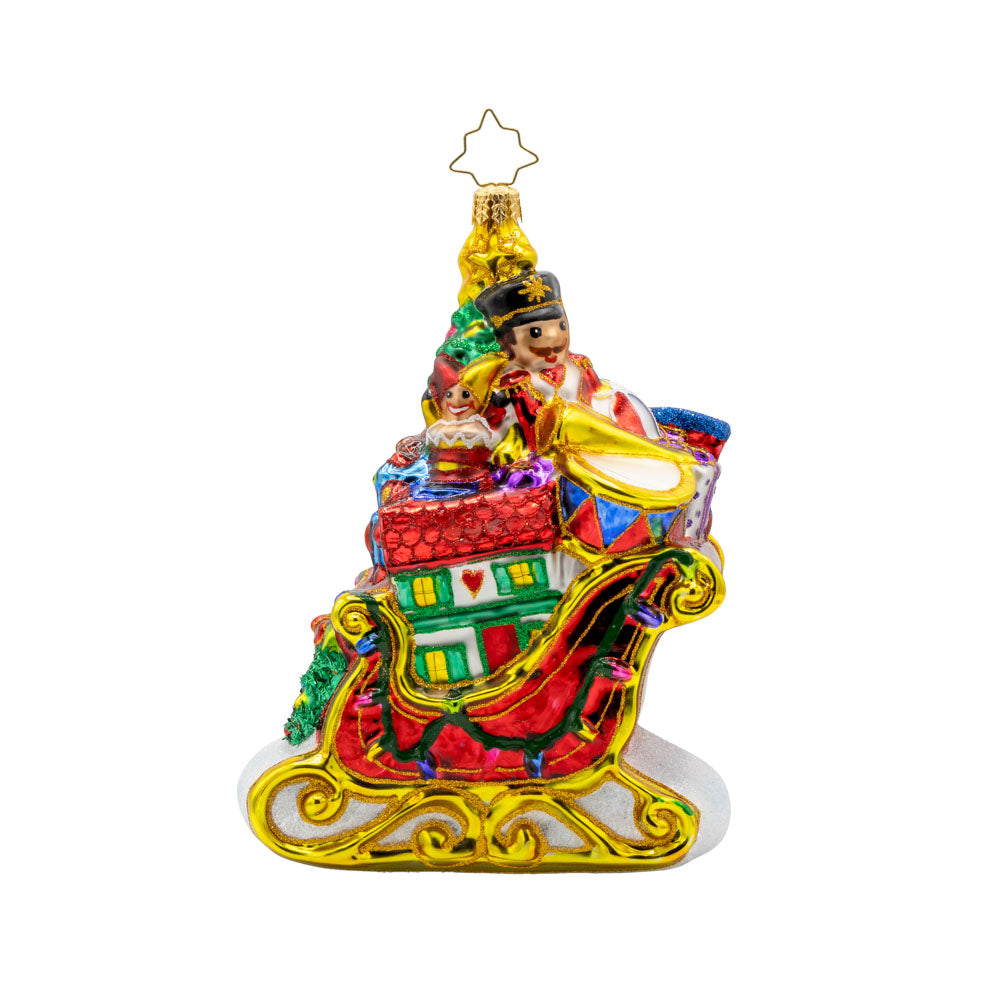 Jolly Sleigh Express ornament. A teddy bear, toy soldier, doll house, drum set, robot, rocking horse, and train engine are seen amidst the pile of presents in the sleigh. A Christmas tree is included in this festive scene. View of back.