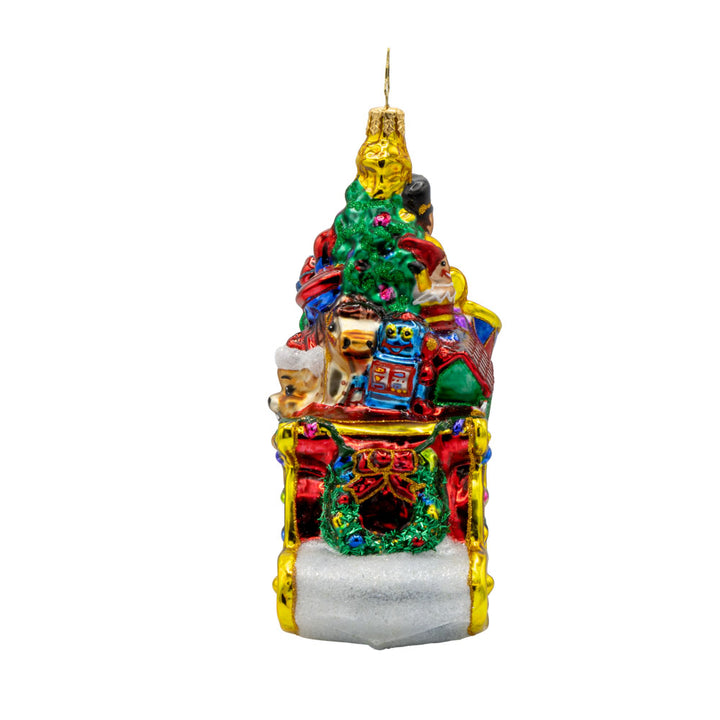 Jolly Sleigh Express ornament. A teddy bear, toy soldier, doll house, drum set, robot, rocking horse, and train engine are seen amidst the pile of presents in the sleigh. A Christmas tree is included in this festive scene. View of right side.