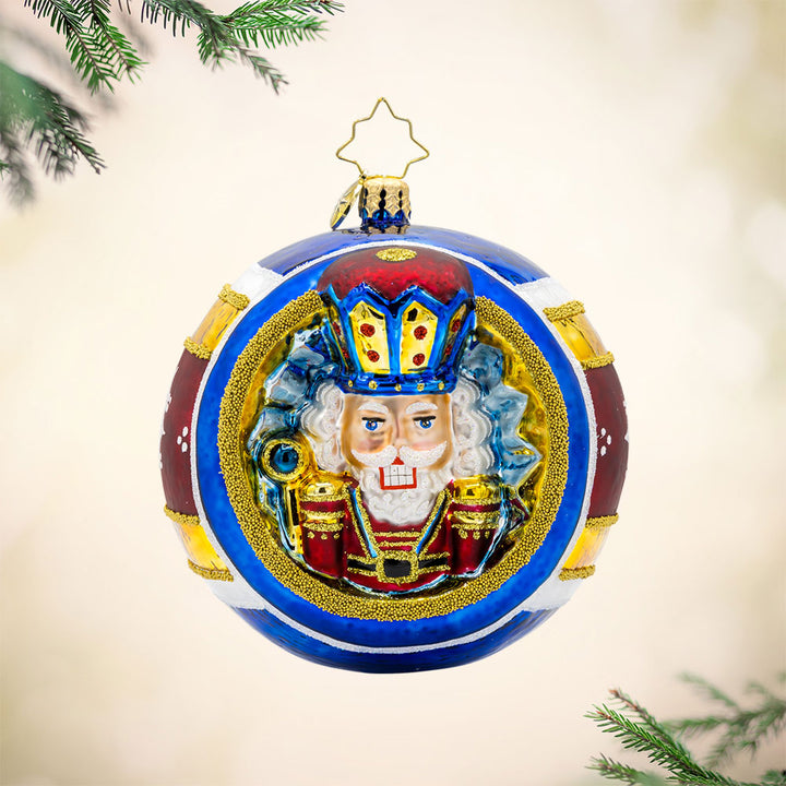 Nutcracker Spherical Splendor ornament. The ornament round features a nutcracker wearing red, blue, and gold, surrounded by painted stripes of the same colors. View of front.