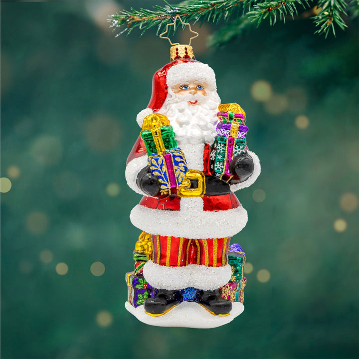 Santa's Stocking Stuffers ornament. Santa wearing his classic red suit, has presents stacked in both arms and around his feet. View of front.