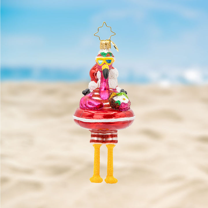 Floatin' Flamingo Fun ornament. Features a flamingo relaxing on a Santa tube, sipping from a coconut. View of front. 