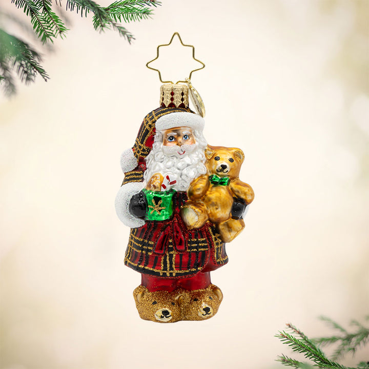 Sweet Slumber Treat Gem ornament. Santa is seen dressed in a plaid red, gold, and black robe. Tedd bear in hand and a mug of hot cocoa in the other. View of front. 