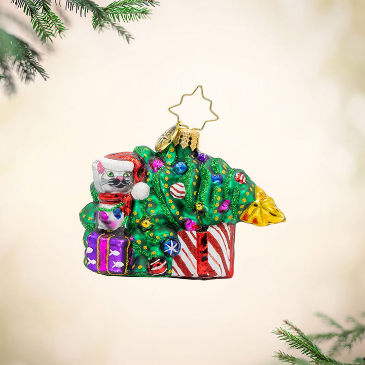 Festive Feline Fiasco Gem ornament. A grey cat sits on top of a present next to a half-fallen decorated Christmas tree. View of front. 