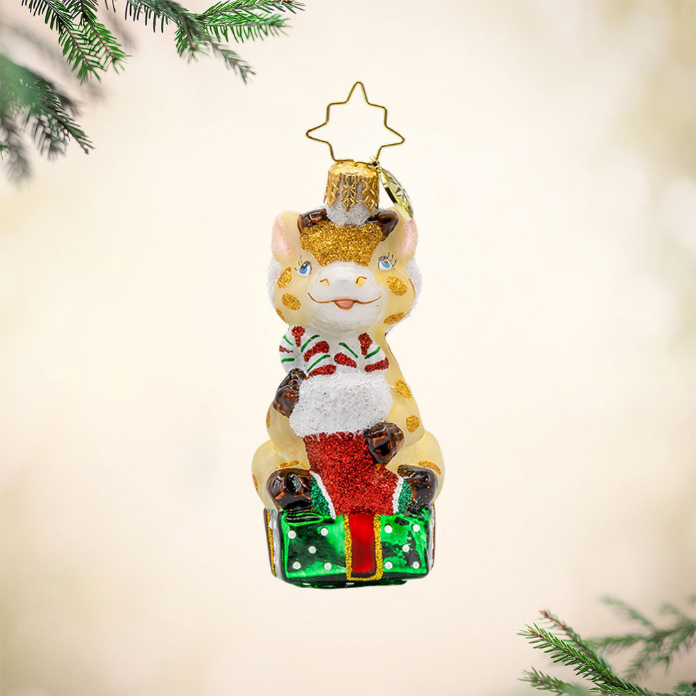 Stacked with Sweetness Gem ornament. A giraffe sits atop a gift with a stocking full of candy canes in hand. View of front. 