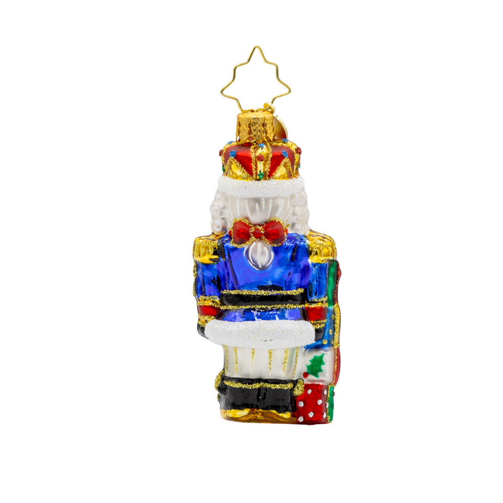 Royal Gift Guardian 2025 Gem ornament. This nutcracker dons a suit of blue, red, and gold, standing next to stacked gifts dated "2025." View of back.