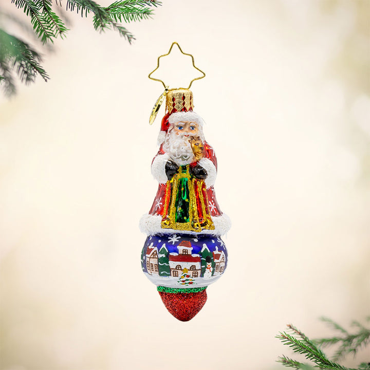 Santa's Splendid Snowscape Gem ornament. Santa stands atop a hand-painted scene of a snow-covered village. View of front. 
