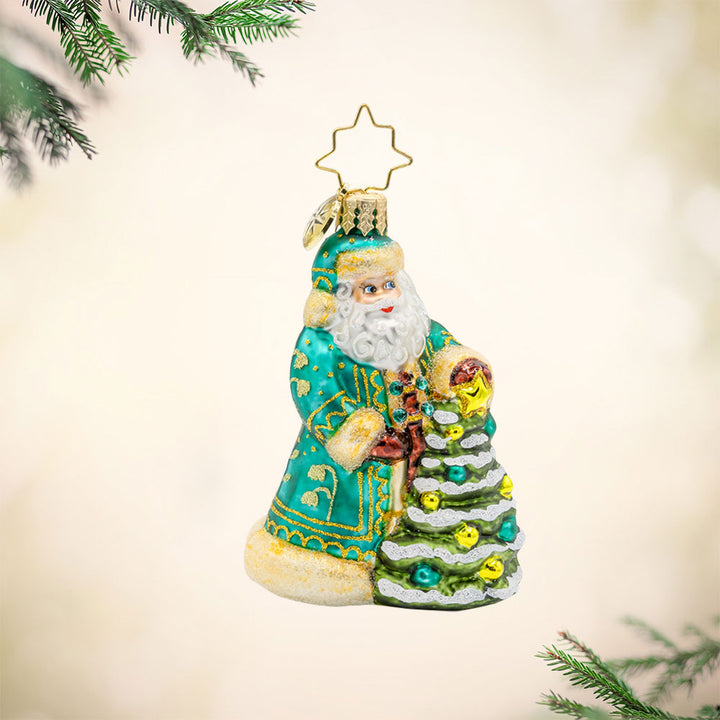 Santa's Tinsel Touch Gem ornament. Santa dons a green and gold intricately detailed robe as he tends to a tiny Christmas tree. View of front. 