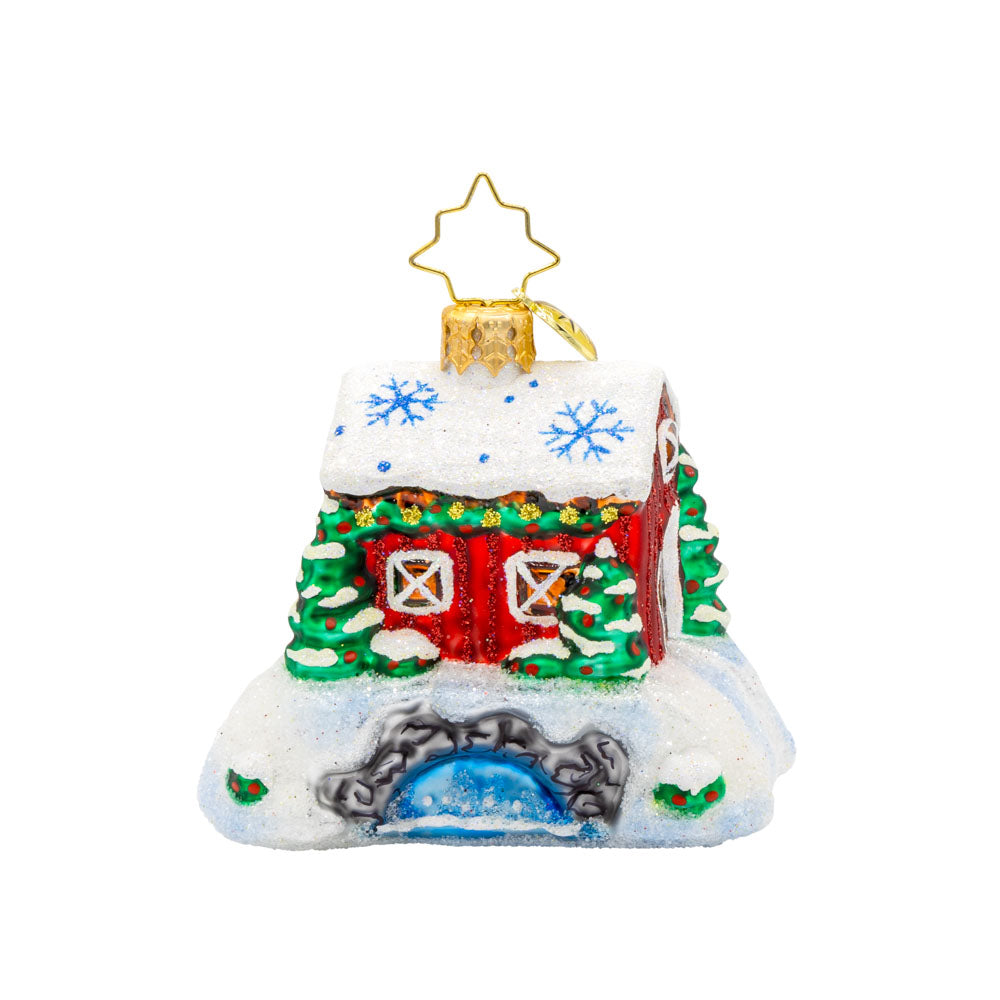 A New England Crossing Gem ornament. A red cabin covered in snow and festive greens sits atop a stone bridge, water rushing underneath. View of back.