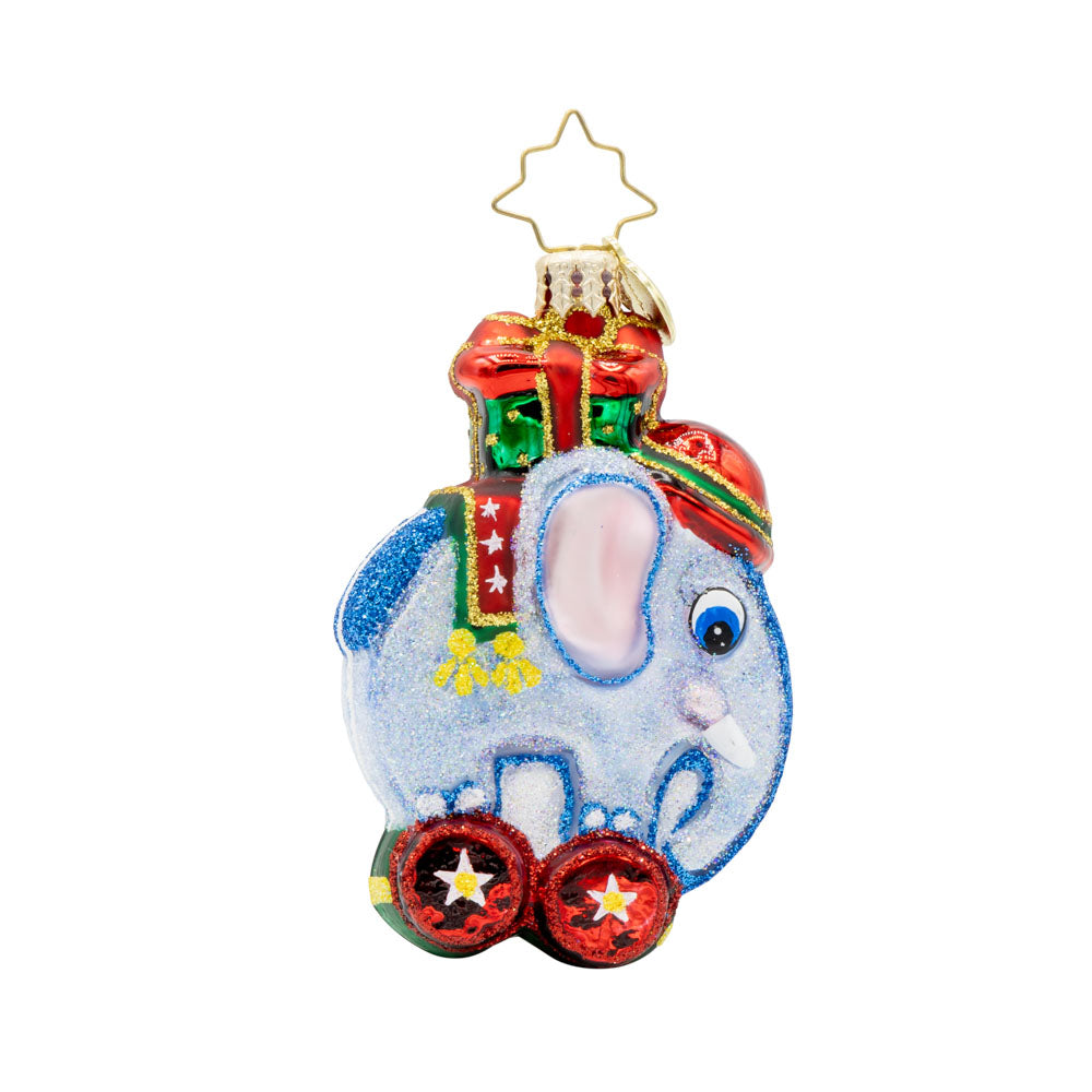 Tiny Trunk Traveler Gem ornament. A blue toy elephant with a gift atop its back, standing on two red wheels. View of front.