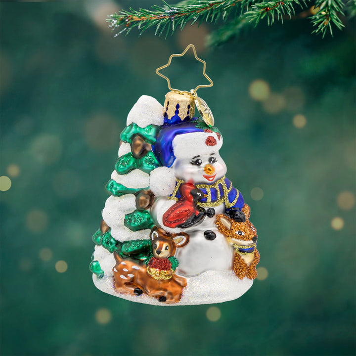 Wintery Pals Gem ornament. A snowman is seen with his forest friends in front of a pine tree covered in snow. View of front. 