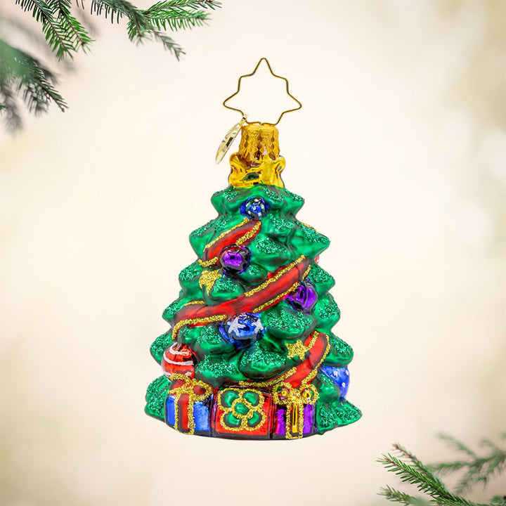 Wintery Tannenbaum Gem ornament. A decorated Christmas tree wrapped with a red ribbon. Gifts sit under the tree. View of front. 