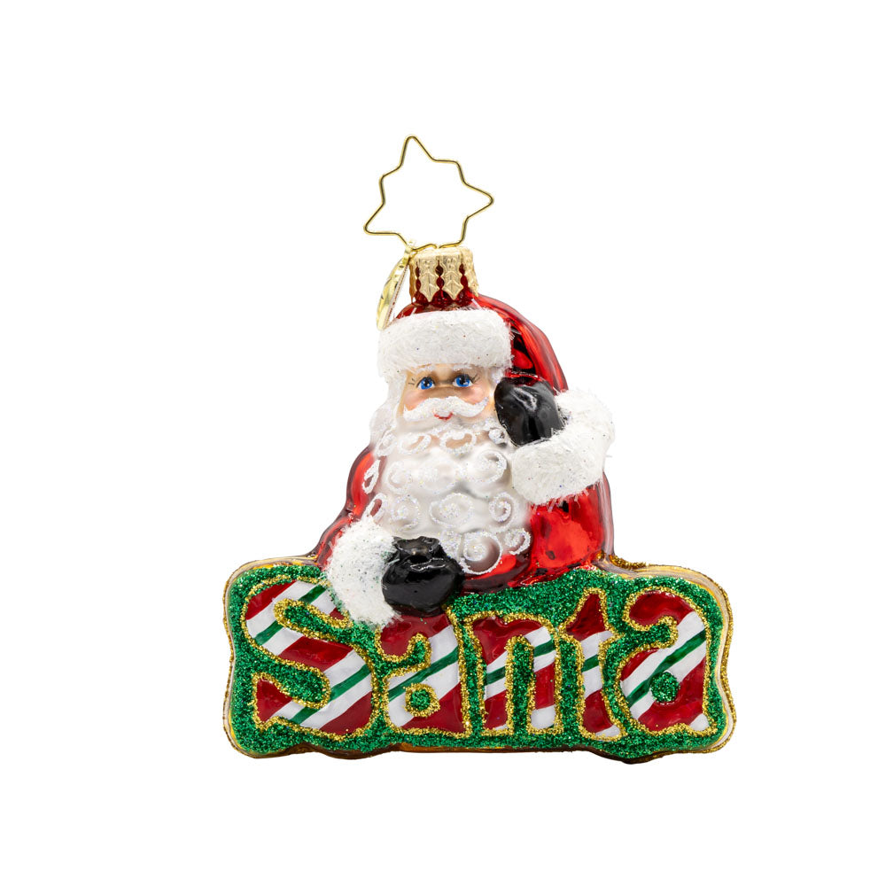 What’s in A Name Santa Gem ornament. Santa leans atop a green and red striped festive "Santa." View of front. 