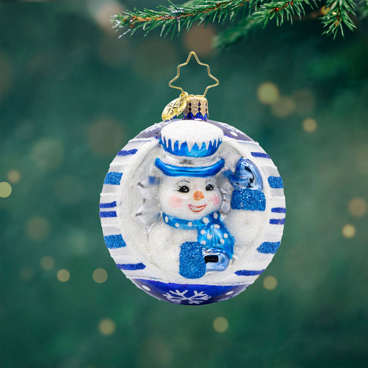 Snowy Spherical Cheer Gem ornament. A snowman dressed in a blue hat, scarf, and mittens. Encircled in a white ornament with blue stripes. View of front. 