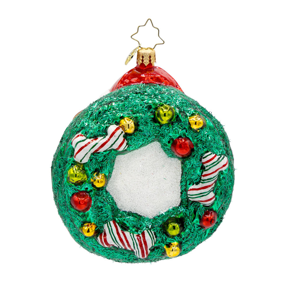 Merry Dogmas ornament. Features a pup wearing a Santa hat, encircled by a wreath and festive bones. View of back.