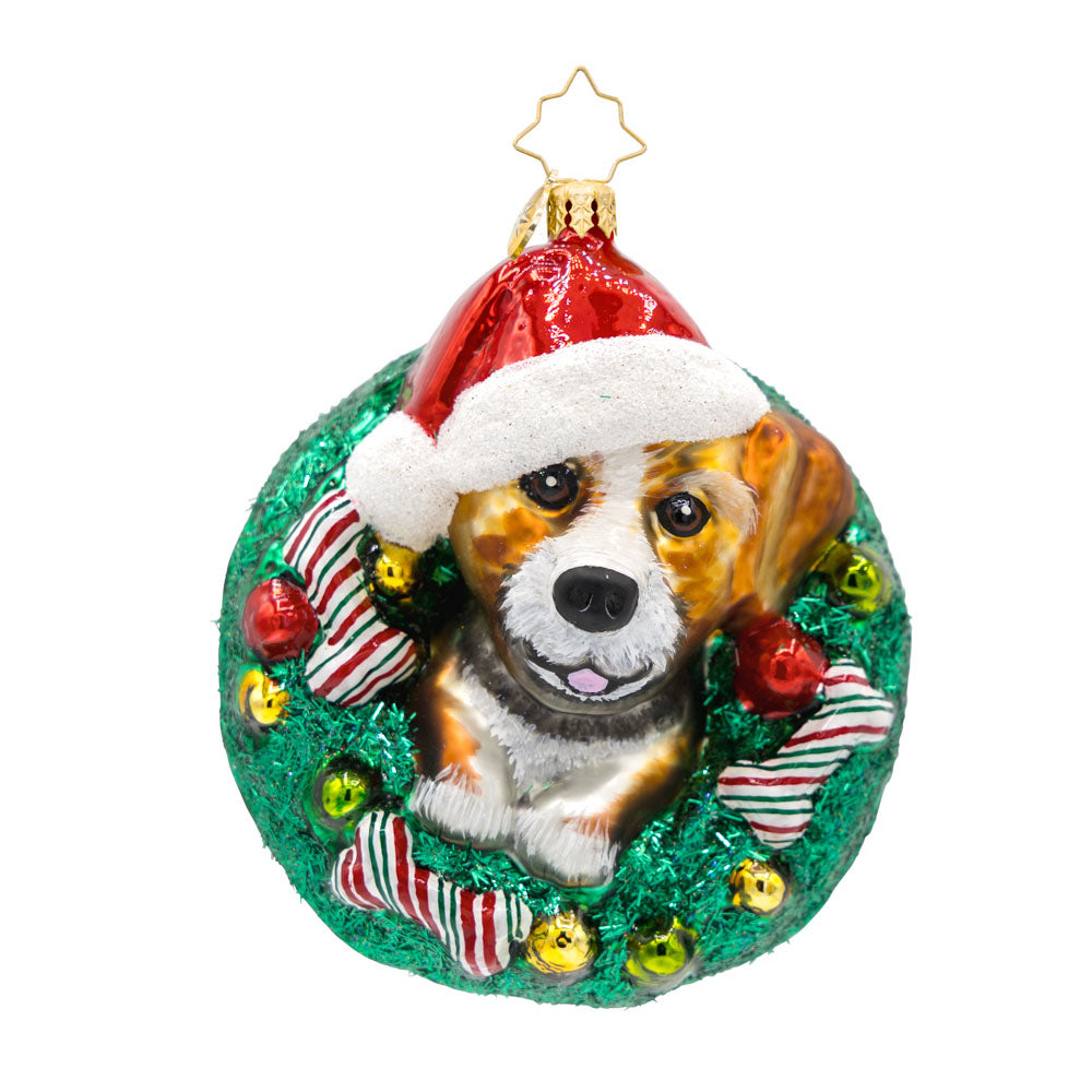 Merry Dogmas ornament. Features a pup wearing a Santa hat, encircled by a wreath and festive bones. View of front. 