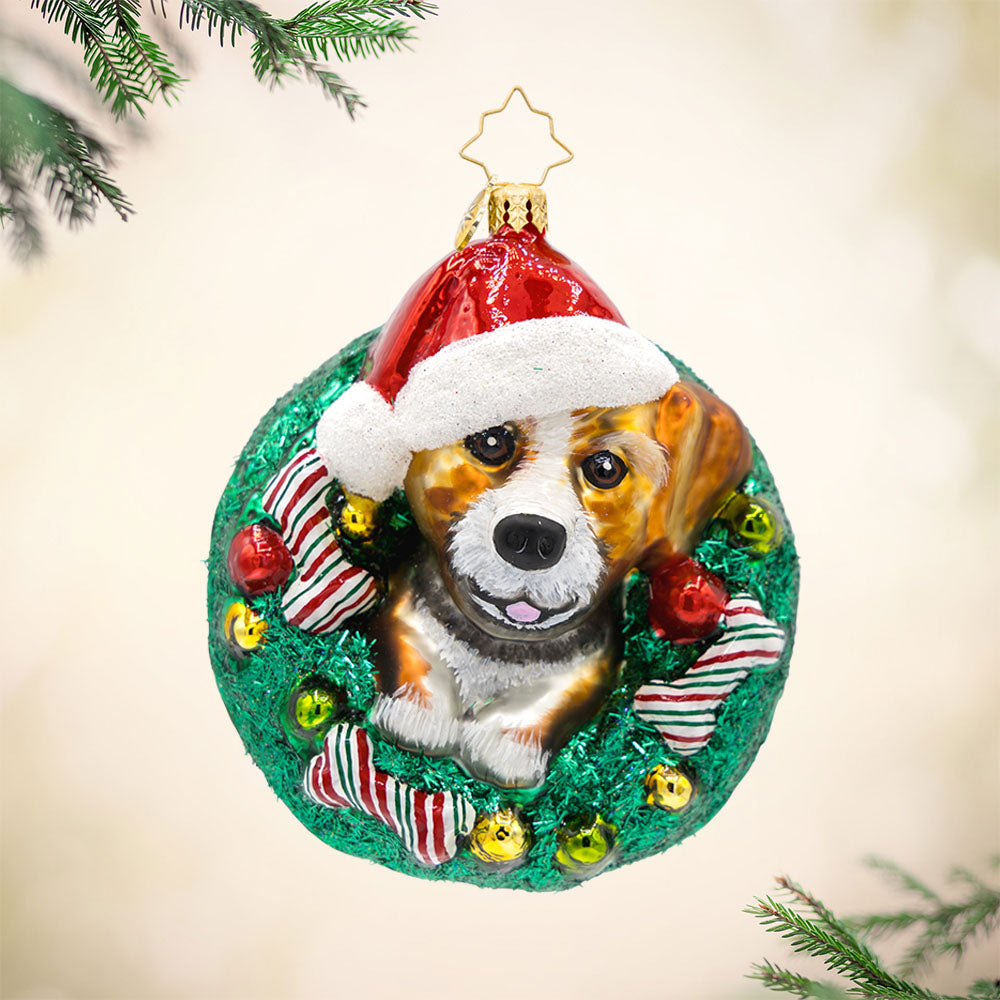 Merry Dogmas ornament. Features a pup wearing a Santa hat, encircled by a wreath and festive bones. View of front. 