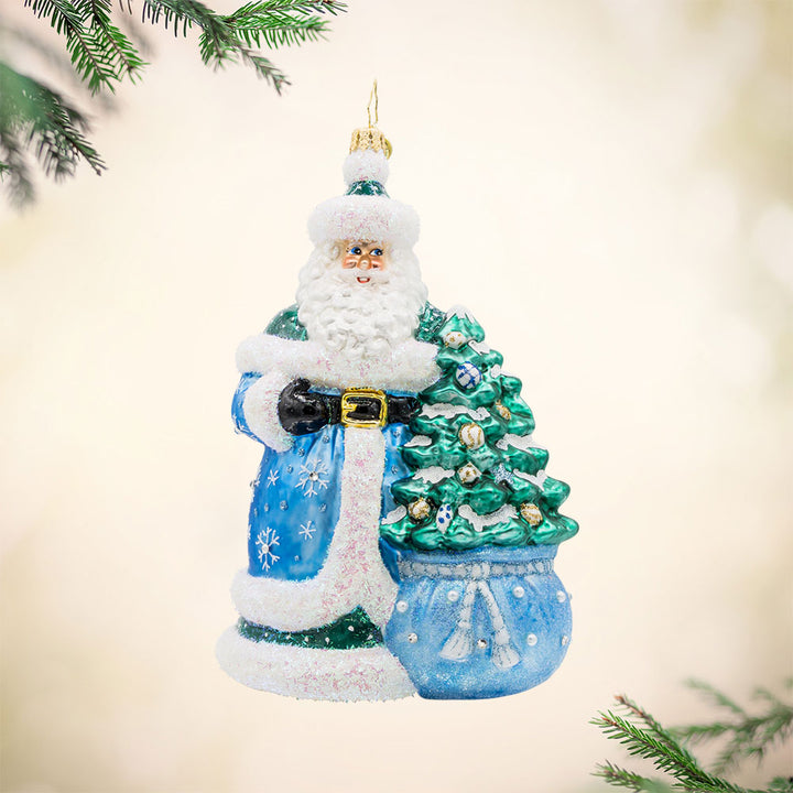 Christmas Enchanted Santa ornament. Santa dons' festive colors with sparkling details. A decorated Christmas tree is seen coming out of his gift sack. View of front. 