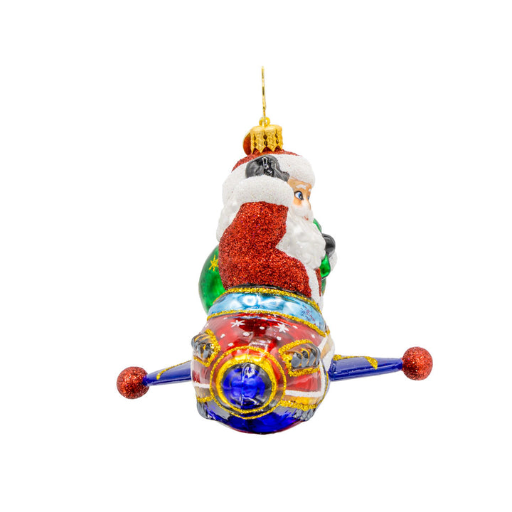 St. Nick's Yuletide Blast ornament. Santa rides in a rocket ship with a green gift sack in hand. View of left side.