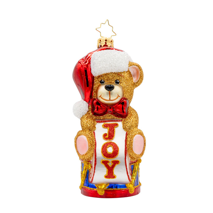 Teddy Bear Greetings ornament. Teddy bear wearing a Santa hat sitting atop a drum holding a sign that says "JOY." View of front. 