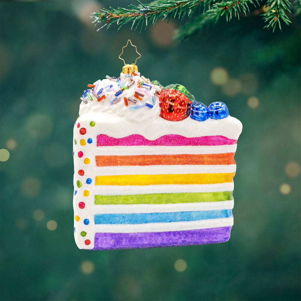 Slice of Joy ornament. A tall slice of rainbow layered cake with sprinkles and fruit on top. View of front. 