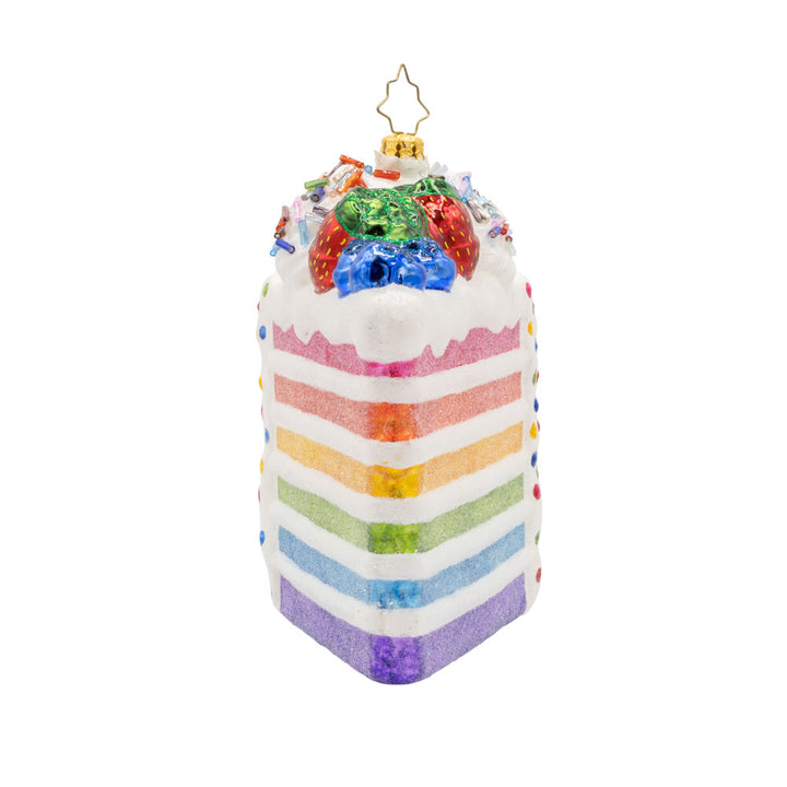 Slice of Joy ornament. A tall slice of rainbow layered cake with sprinkles and fruit on top. View of right side.