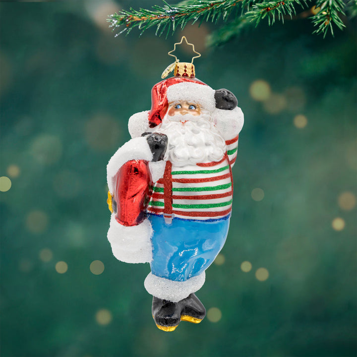Santa's Wardrobe Change ornament. Santa is holding his freshly tailored suit, with a twinkle in his eye and a mischievous grin. View of front. 