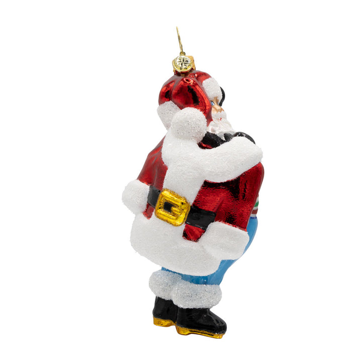 Santa's Wardrobe Change ornament. Santa is holding his freshly tailored suit, with a twinkle in his eye and a mischievous grin. View of left side.