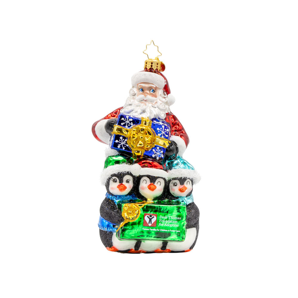 Santa Flurry Friends ornament. Santa is standing with three penguins in front of him, holding a gift with the Dave Thomas Foundation for Adoption logo on the front of it. View of front. 