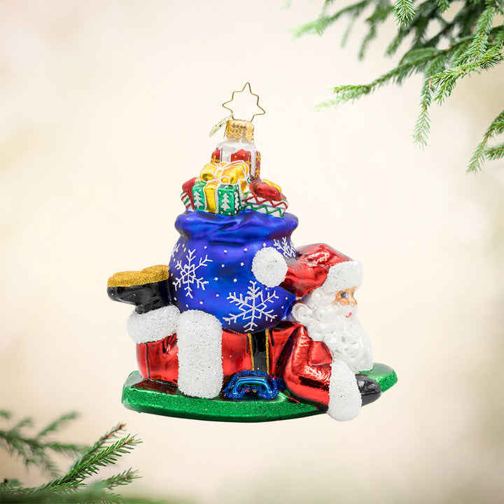 Snowy Sleigher ornament. Dressed in his red suit, Santa is perched on his sled, with a gift sack of presents on his back. View of front. 