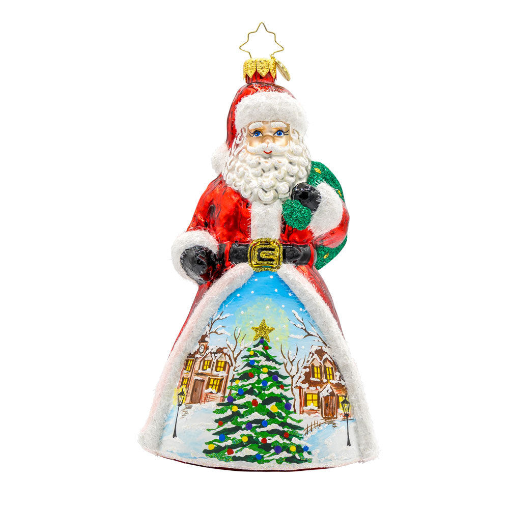 St. Nick's Winter Wonderland ornament. Santa stands amidst a picturesque snowy village. The hand-painted scene features twinkling lights and cozy homes surrounding a Christmas tree in the center. View of front.