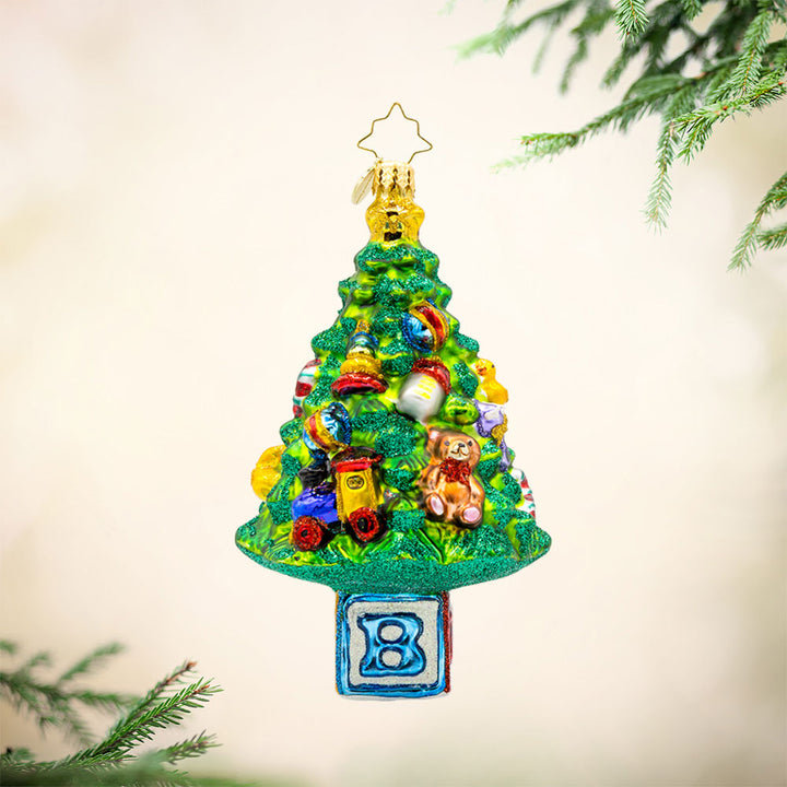 Bundle of Joy Spruce ornament. This piece features a decorated Christmas tree and a collection of baby-themed toys. View of front.